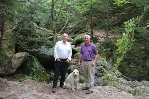 Naugatuck Mayor N. Warren ‘Pete’ Hess, left, Tax Collector Jim Goggin and Hess’ dog, Beau, stop in front of a waterfall along a trail in the Naugatuck State Forest on Aug. 31. The trail, which the borough has been working on since the winter, is part of the 22 kilometer hike that Hess will lead on Sept. 24. –LUKE MARSHALL 
